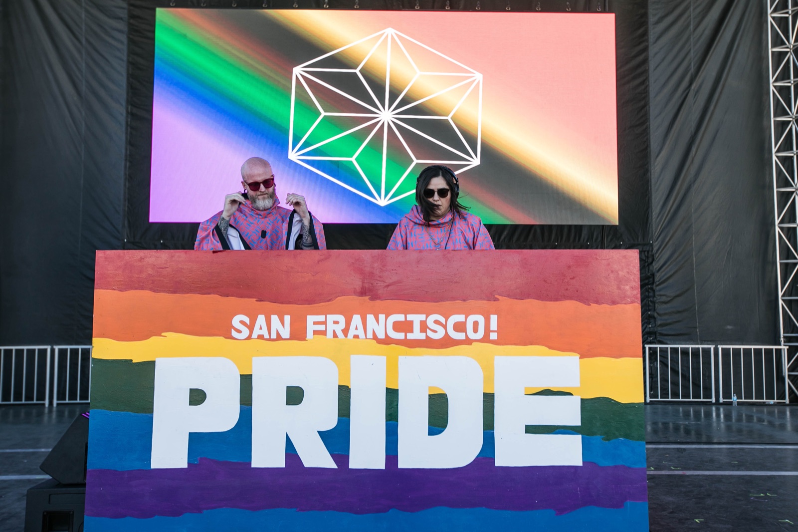 Josette Melchor and John Major (JMxJM) DJing behind a rainbow San Francisco Pride booth on the main stage.